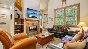 A living room with a fireplace, leather sofas, a coffee table, and a large window with blinds.