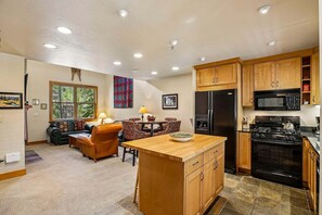 A kitchen with wooden cabinets, a refrigerator, a microwave, and a stove. There is a dining area with a table and chairs.