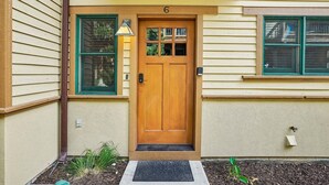 A wooden front door with a number '6' above it, a green-framed window to the left, and a small mailbox on the right.
