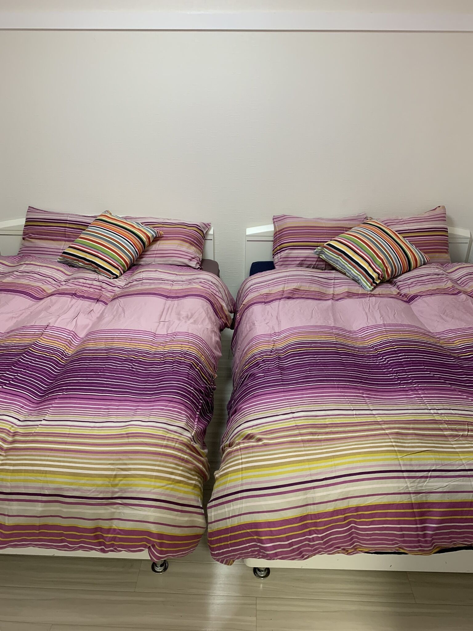 Uma cama de casal com colcha listrada e travesseiros, uma mesa de cabeceira e uma parede lisa.
