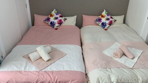 A double room with two beds, each with a pink and white bedspread, floral pillows, and neatly folded towels. - GOLDHOUSE Shinosaka 305 (Osaka)