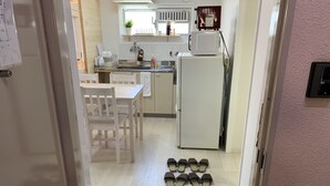 A kitchen with white cabinets, a microwave, and a refrigerator. There is a table with chairs and a sink. Shoes are placed on the floor. - GOLDHOUSE Shinosaka 305 (Osaka)