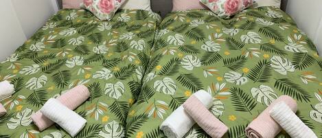 A double bed with floral and leaf-patterned bedding, two pillows, and rolled towels.