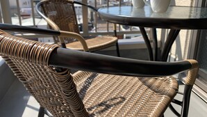 A wicker chair with a black armrest, a round table with a white mug, and a view of buildings through a window. - A-Style Matsu 601 (Osaka)