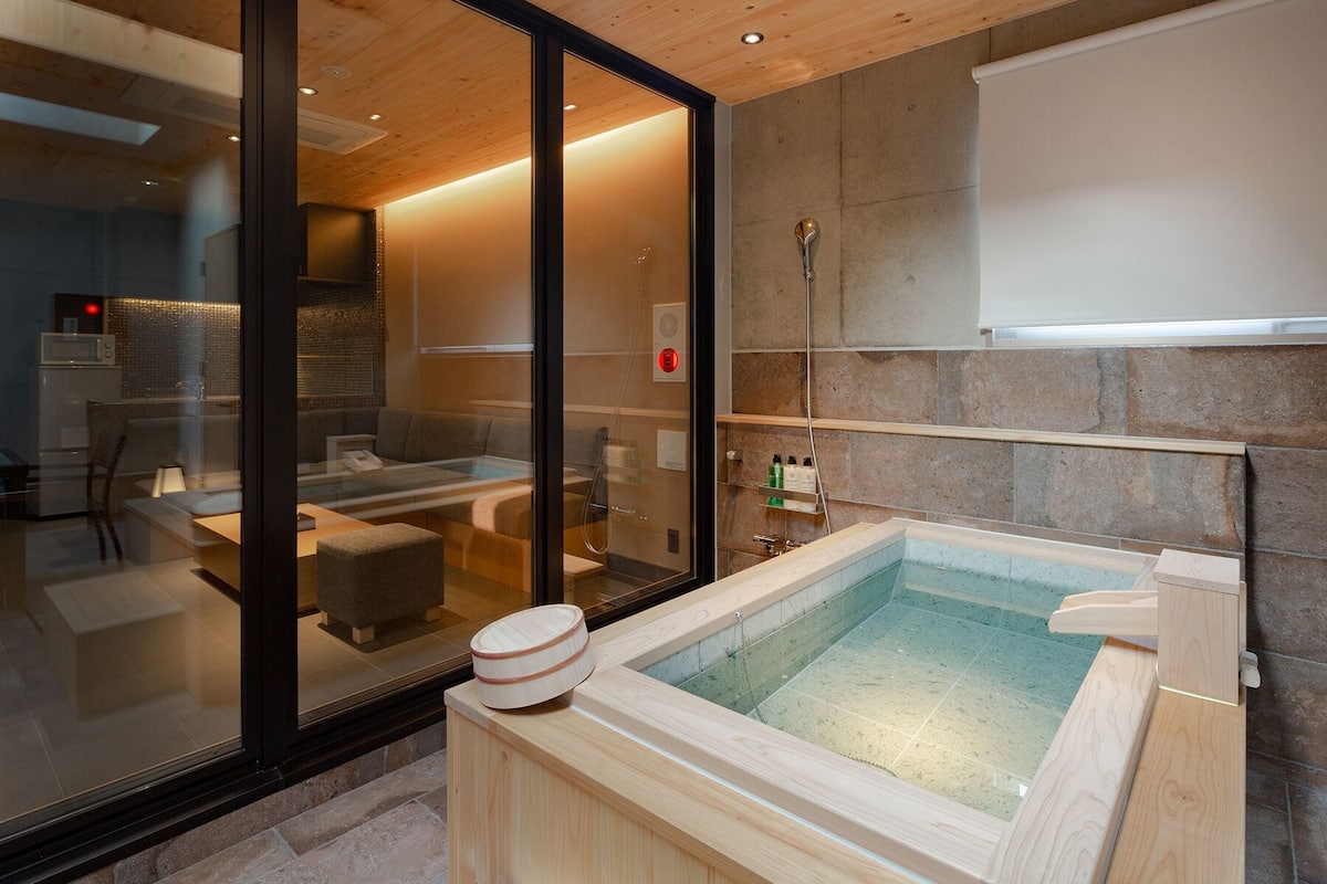 A modern spa room with a glass-enclosed seating area, a wooden sauna, and a stone wall.
