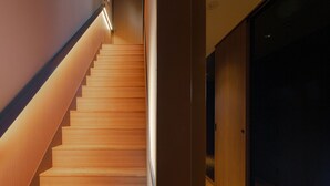 Una escalera moderna con escalones de madera y una barandilla iluminada, que conduce a una habitación oscura.