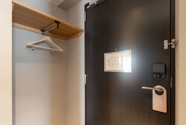Une chambre d’hôtel avec une porte en bois sombre, une petite fenêtre, un interphone et un porte-manteau mural.