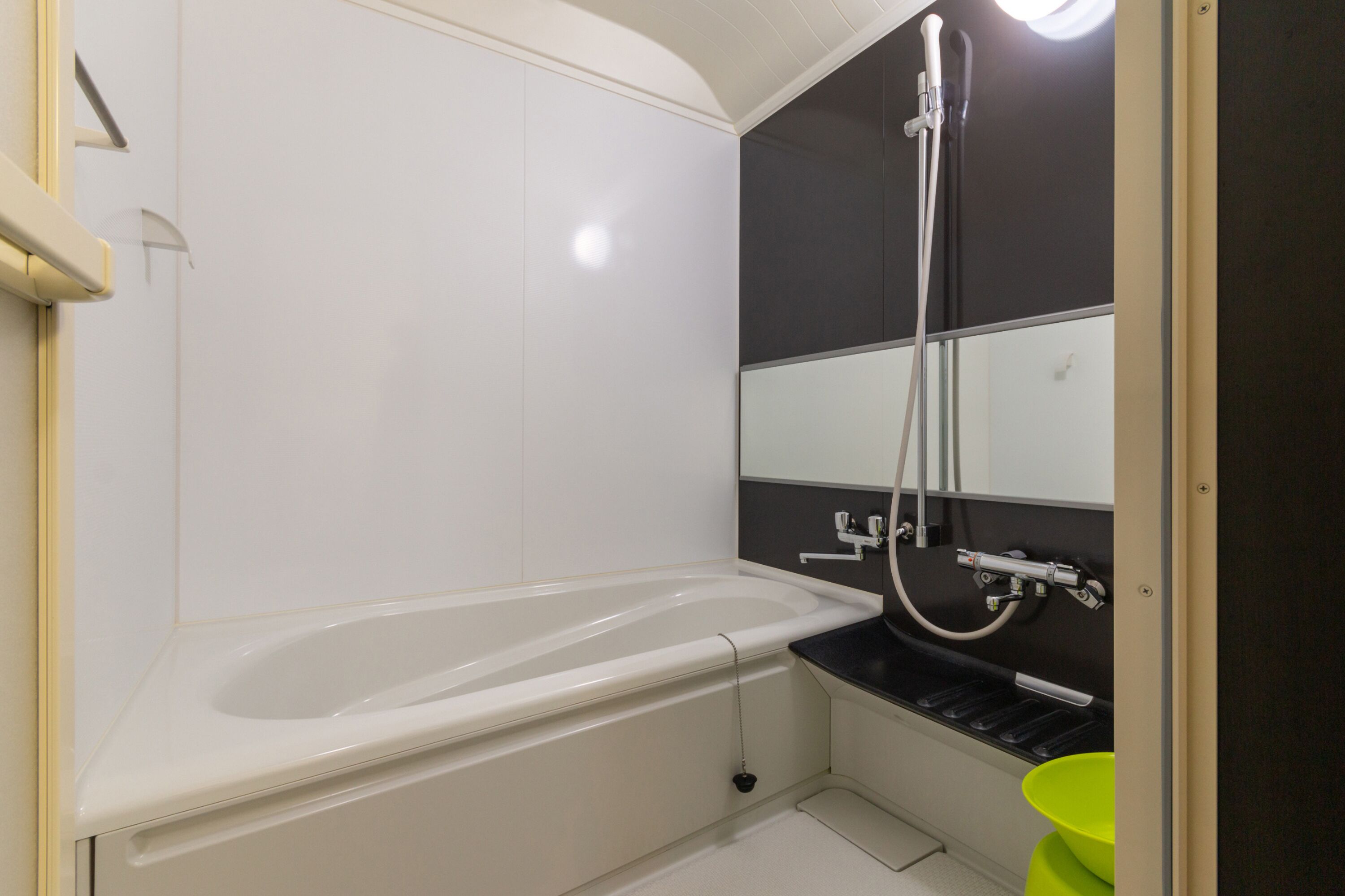 A small, modern bathroom with a white bathtub, a showerhead, and a green bucket.