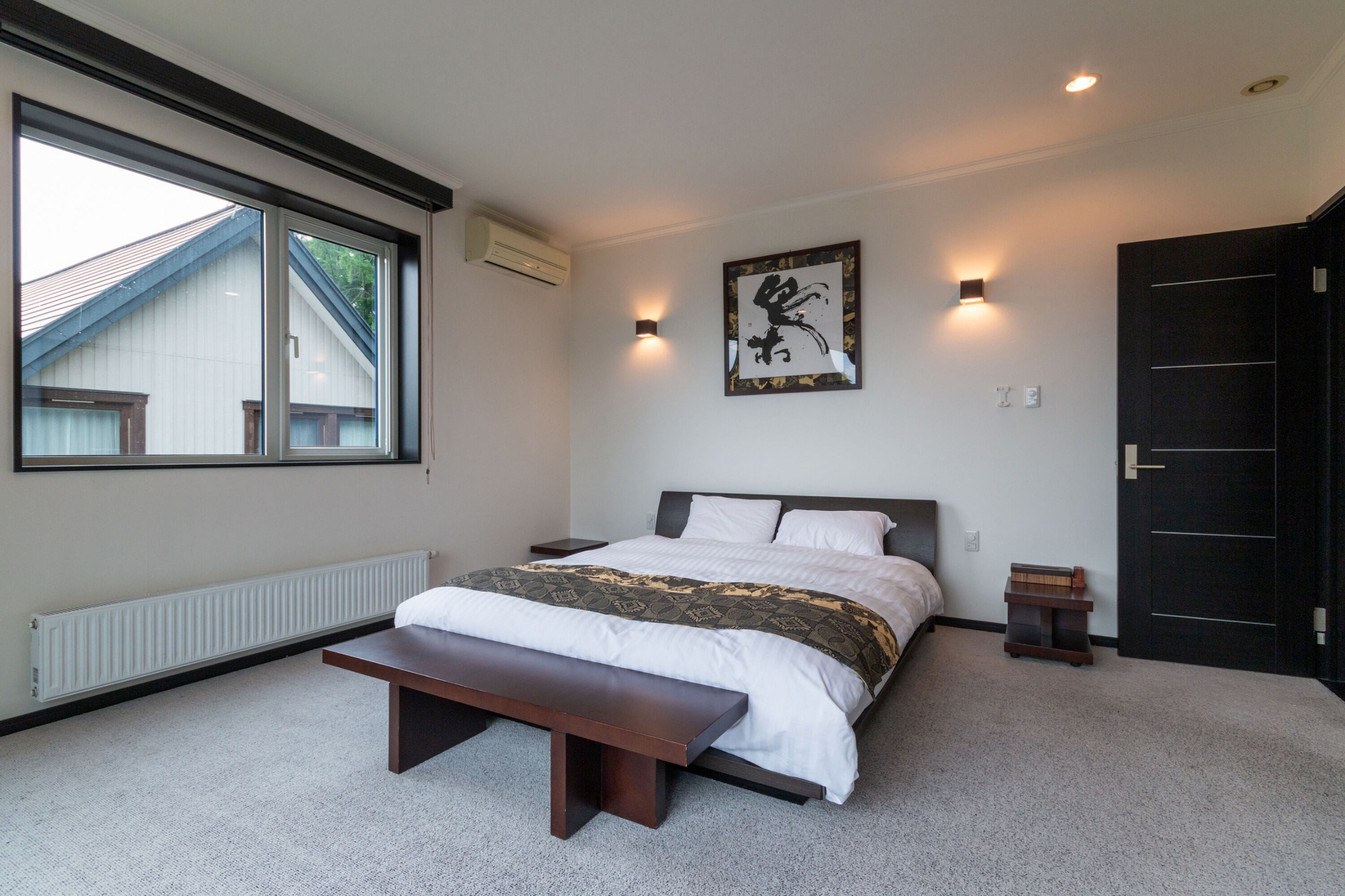 A bedroom with a large bed, a bench, a window, and a door.