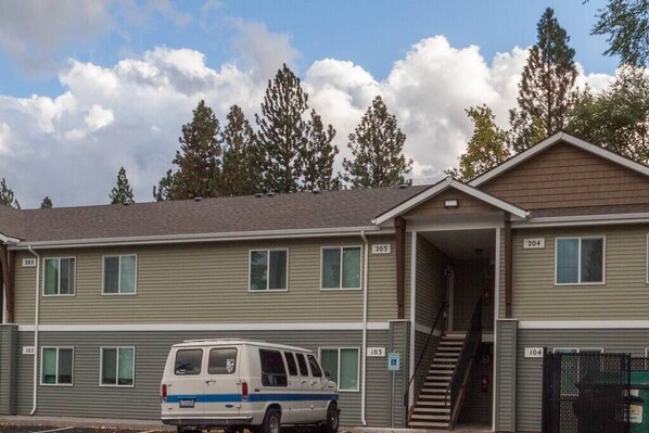 A multi-story building with numbered doors, a van parked in front, and a staircase leading to the entrance.