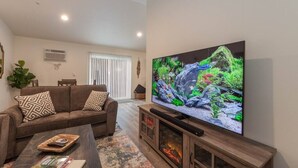Una sala de estar con un televisor de pantalla plana grande, un sofá con cojines estampados, una mesa de centro y una chimenea.