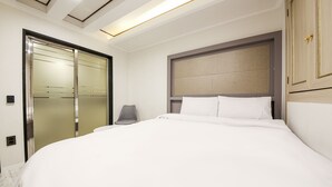 A modern hotel room with a large bed, a grey chair, a wardrobe with frosted glass doors, and a ceiling with recessed lighting. - Diamond Hotel (Jinju)