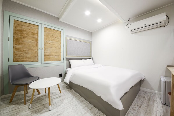 A bedroom with a bed, a chair, a small table, an air conditioning unit, and a wardrobe. - Diamond Hotel (Jinju)
