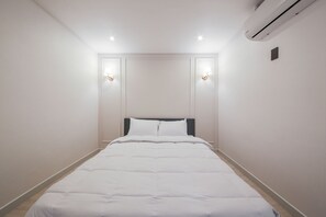 A neatly made bed in a hotel room with a headboard, two wall-mounted lights, and an air conditioning unit on the wall. - Boutique Hotel Super Rocket (Jinju)