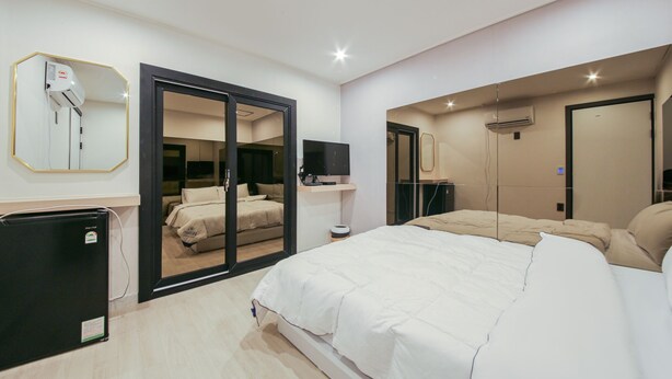 Een moderne slaapkamer met een groot bed, een kledingkast met schuifdeur, een klein bureau en een spiegel aan de muur.