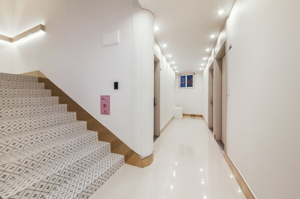 A modern hotel hallway with a patterned carpeted staircase, a clean floor, and a bright, well-lit corridor. - Boutique Hotel Super Rocket (Jinju)