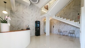 Een hotellobby met een marmeren wand, een receptiebalie, een digitaal kiosk en een trap.