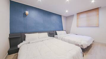A modern hotel room with two beds, a blue accent wall, and a window with blinds.