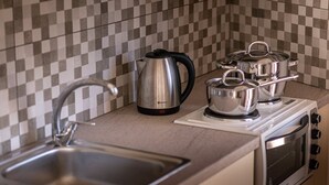 Une cuisine avec un dosseret à carreaux, une bouilloire en acier inoxydable, deux casseroles sur une plaque de cuisson mobile et un évier.
