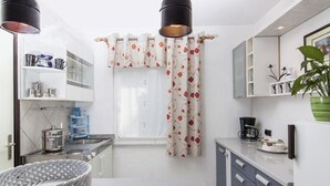 A modern kitchen with white cabinets, a sink, and a stove. There is a window with a floral curtain, and a plant on the counter. - Apartment 418/952 (Istria - Valbandon), 1800m from the beach (Valbandon)