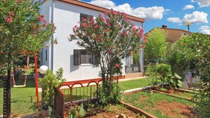 A white building with a red roof, surrounded by a garden with various plants and a swing set. - Apartment 418/952 (Istria - Valbandon), 1800m from the beach (Valbandon)