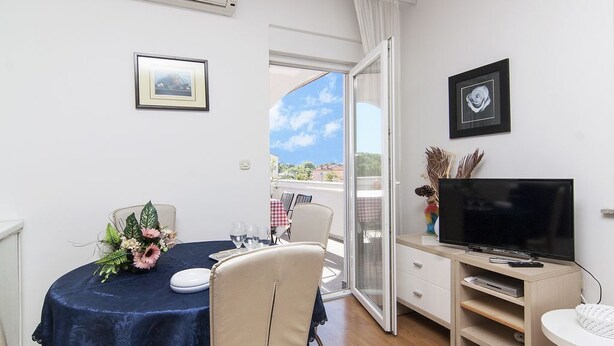 Ein Zimmer mit Esstisch, Stühlen, Fernseher und einem Balkon mit Aussicht.