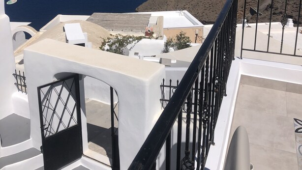 A seaside view from a balcony with white buildings, a clear sky, and a distant coastline. - Doukas Caldera Suites Fira (Santorini)