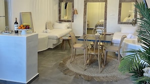 A modern, well-lit room with a dining area, a sofa, and a small table. - Doukas Caldera Suites Fira (Santorini)