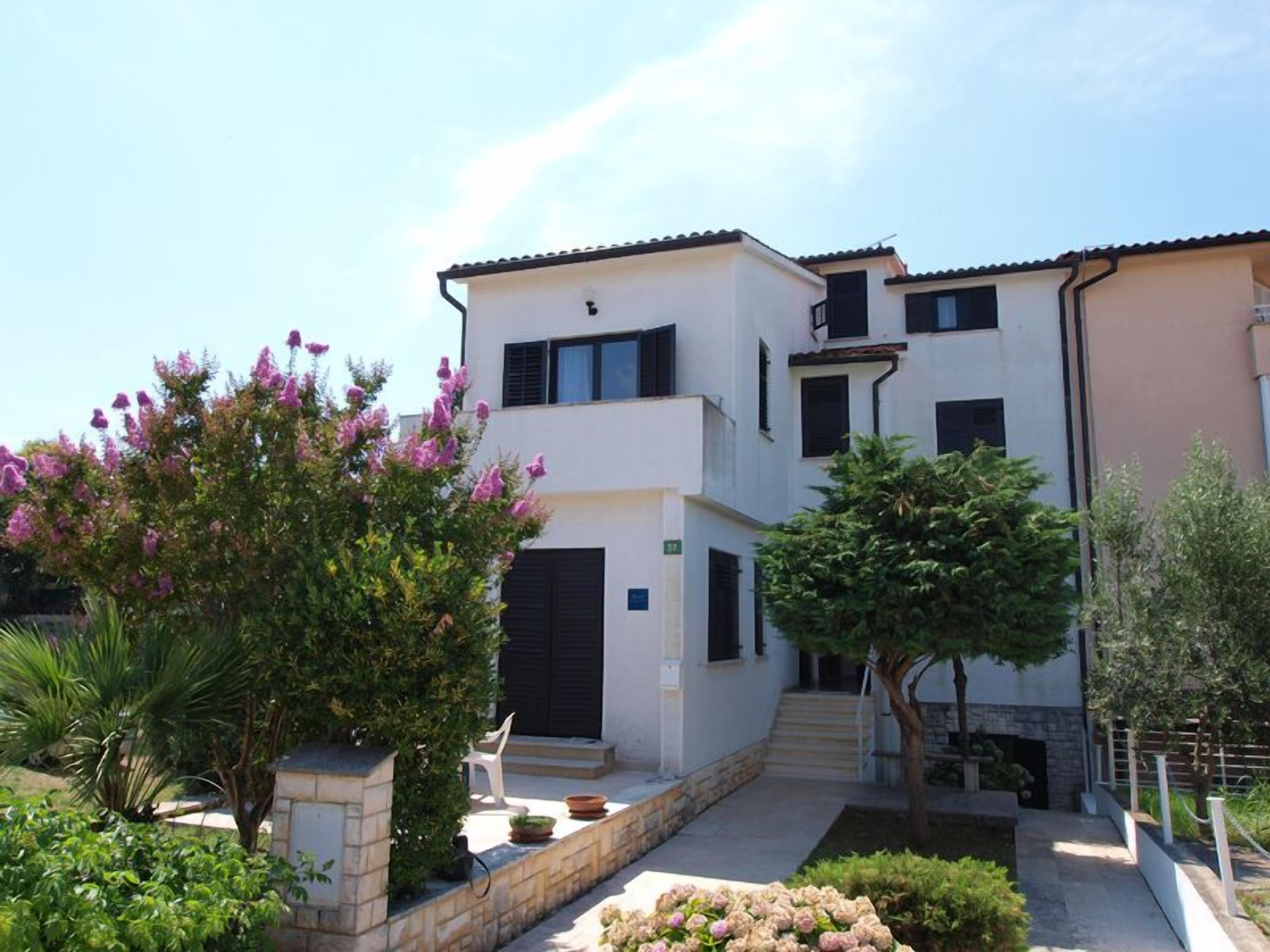 A two-story building with a white facade, black shutters, and a stone pathway leading to the entrance.