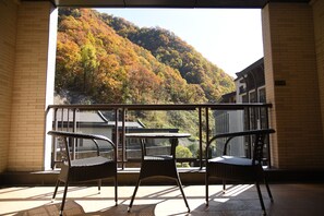 Un balcon avec deux fauteuils en osier et une petite table, donnant sur une colline dont les arbres arborent les couleurs de l’automne.