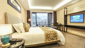 Habitación de hotel con una cama grande, televisión, escritorio y balcón con vista a la ciudad.