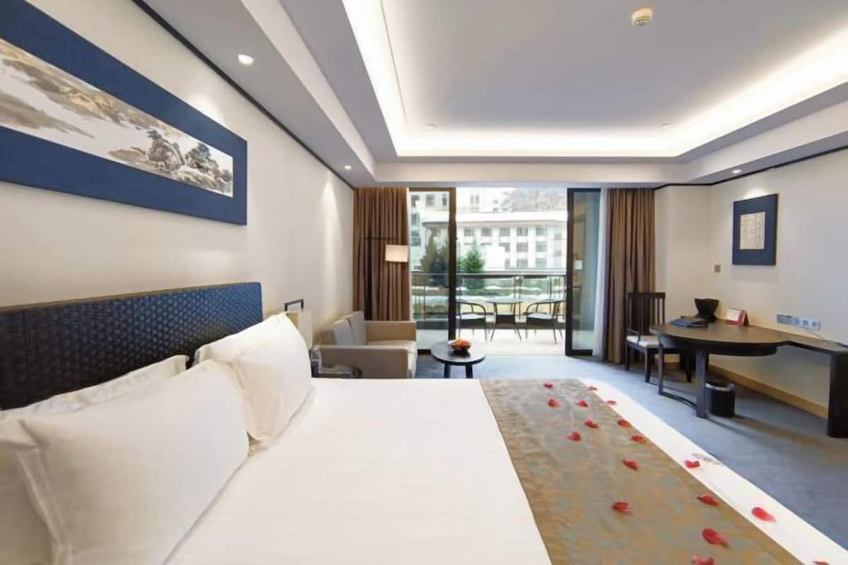 Habitación de hotel con una cama grande, un escritorio, una silla, una mesita y un balcón con vistas a la ciudad.