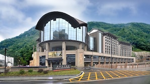 Un hotel moderno con fachada de vidrio curva, una entrada destacada y un paisaje montañoso de fondo.