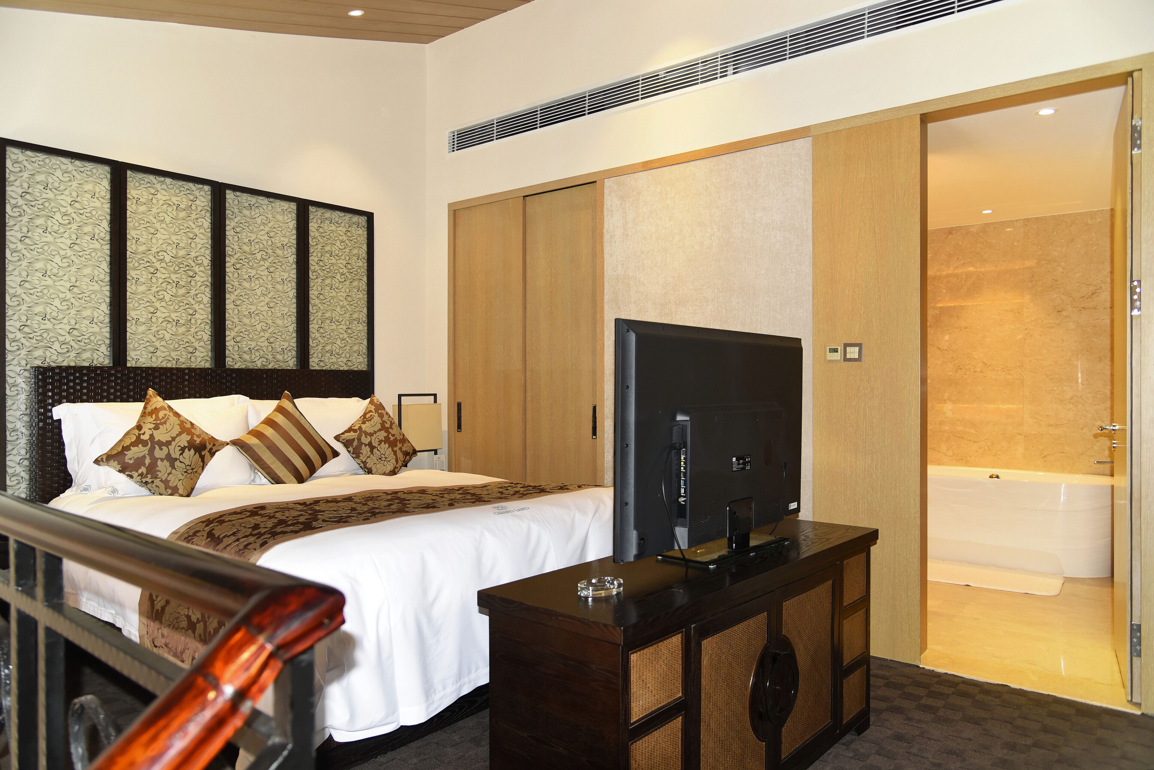A hotel room with a bed, a TV, a wooden wardrobe, and a bathroom with a bathtub.