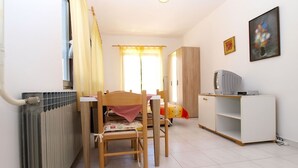 A compact living room with a dining table, two wooden chairs, a white cabinet with a television, and a radiator. - Apartment 727/1701 (Istria - Stinjan), 500m from the beach (Stinjan)