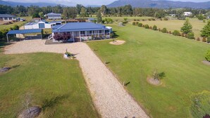 A large building with a blue roof, surrounded by a grassy field and a gravel driveway. - Kulang Lodge - A peaceful getaway on the outskirts of the village (Broke)