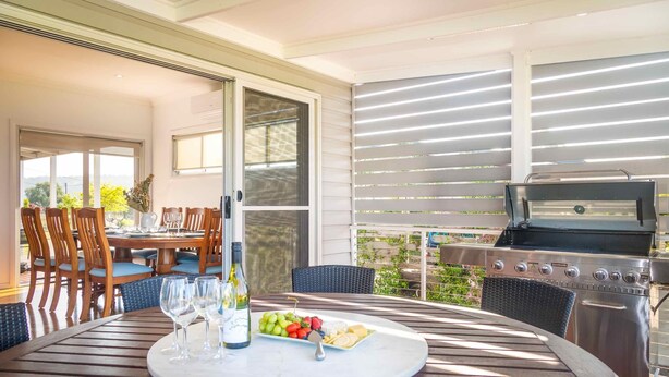 An outdoor dining area with a grill, a table set with wine glasses and a fruit platter, and a view of greenery. - Kulang Lodge - A peaceful getaway on the outskirts of the village (Broke)