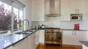 A modern kitchen with stainless steel appliances, white cabinets, and a large window. - Kulang Lodge - A peaceful getaway on the outskirts of the village (Broke)