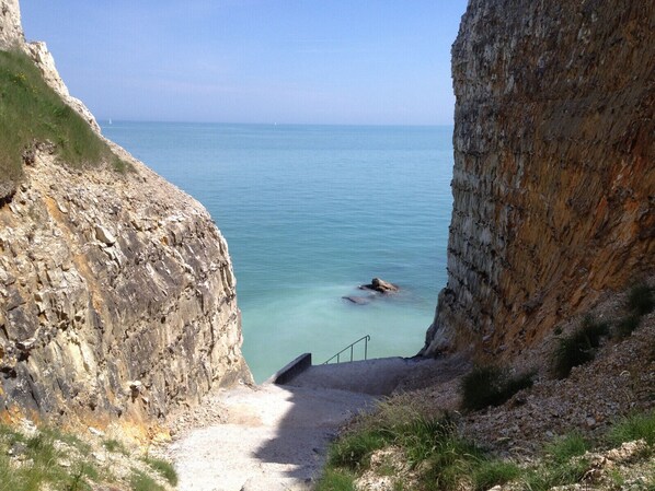 Un sentier côtier menant à une falaise surplombant une mer calme.