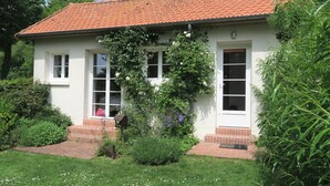 Um edifício branco com telhado de telhas vermelhas, duas janelas e um pequeno jardim com grama e flores.
