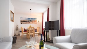 Un salon moderne avec une table basse en verre, un canapé, un coin repas avec des chaises et un téléviseur à écran plat.