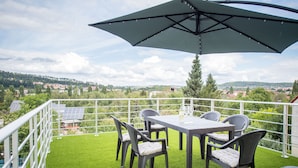 Une terrasse avec une table et des chaises, un grand parasol et une vue sur la ville.