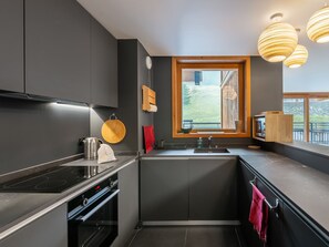 A modern kitchen with dark cabinetry, a built-in oven, a stovetop, and a window with a view of greenery outside.
