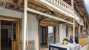 A rustic outdoor dining area with a table set for two, a wooden fence, and a balcony with wooden beams.