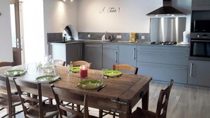 A modern kitchen with grey cabinets, a wooden dining table set with green plates, and a "Table!" sign on the wall.