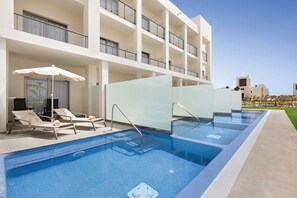 A swimming pool with lounge chairs and umbrellas, surrounded by a building with multiple balconies. - Hotel Riu Palace Santa Maria - All Inclusive (Sal)