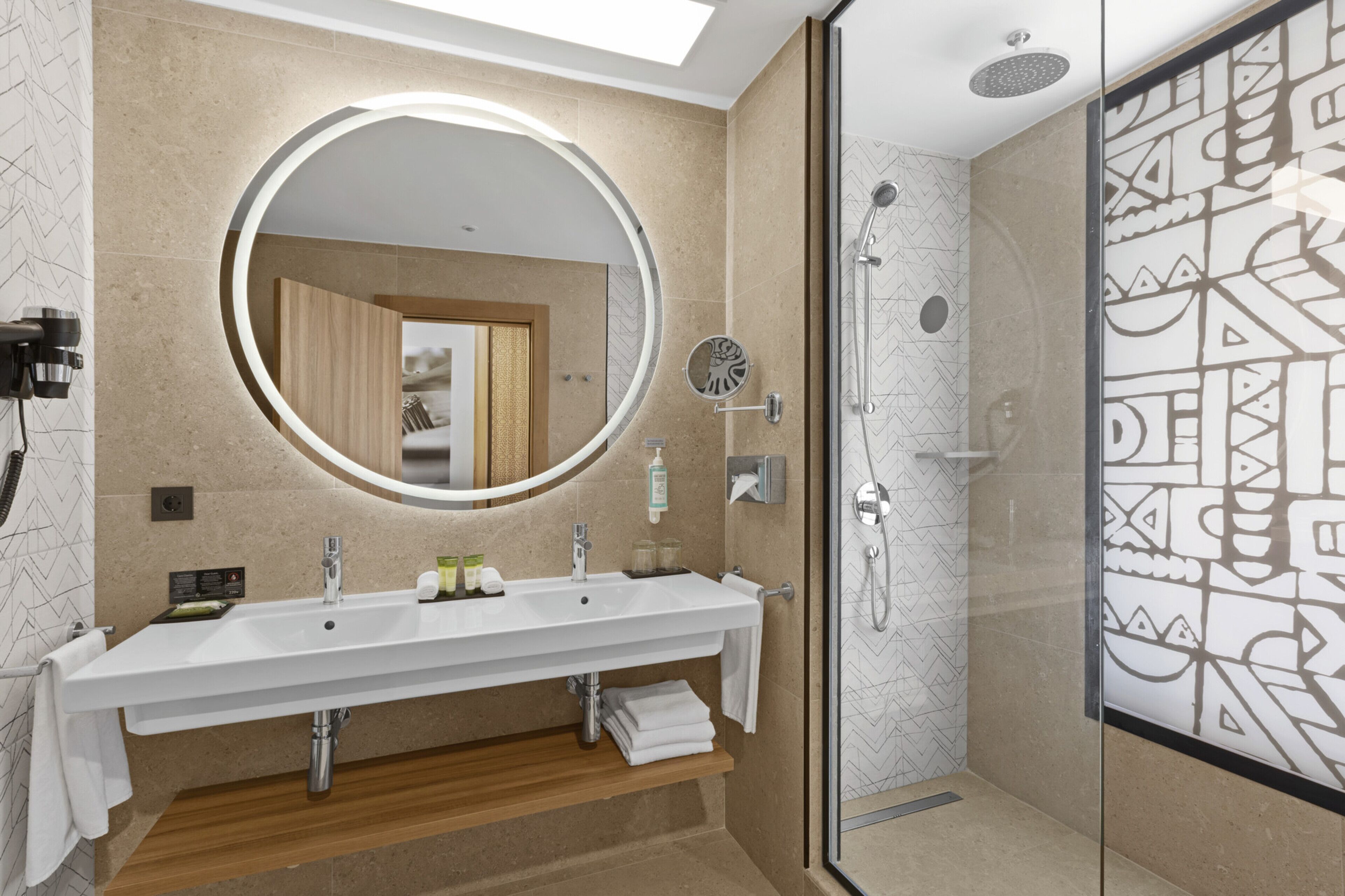 A modern bathroom with a large mirror, two sinks, a shower, and a glass-enclosed shower area.