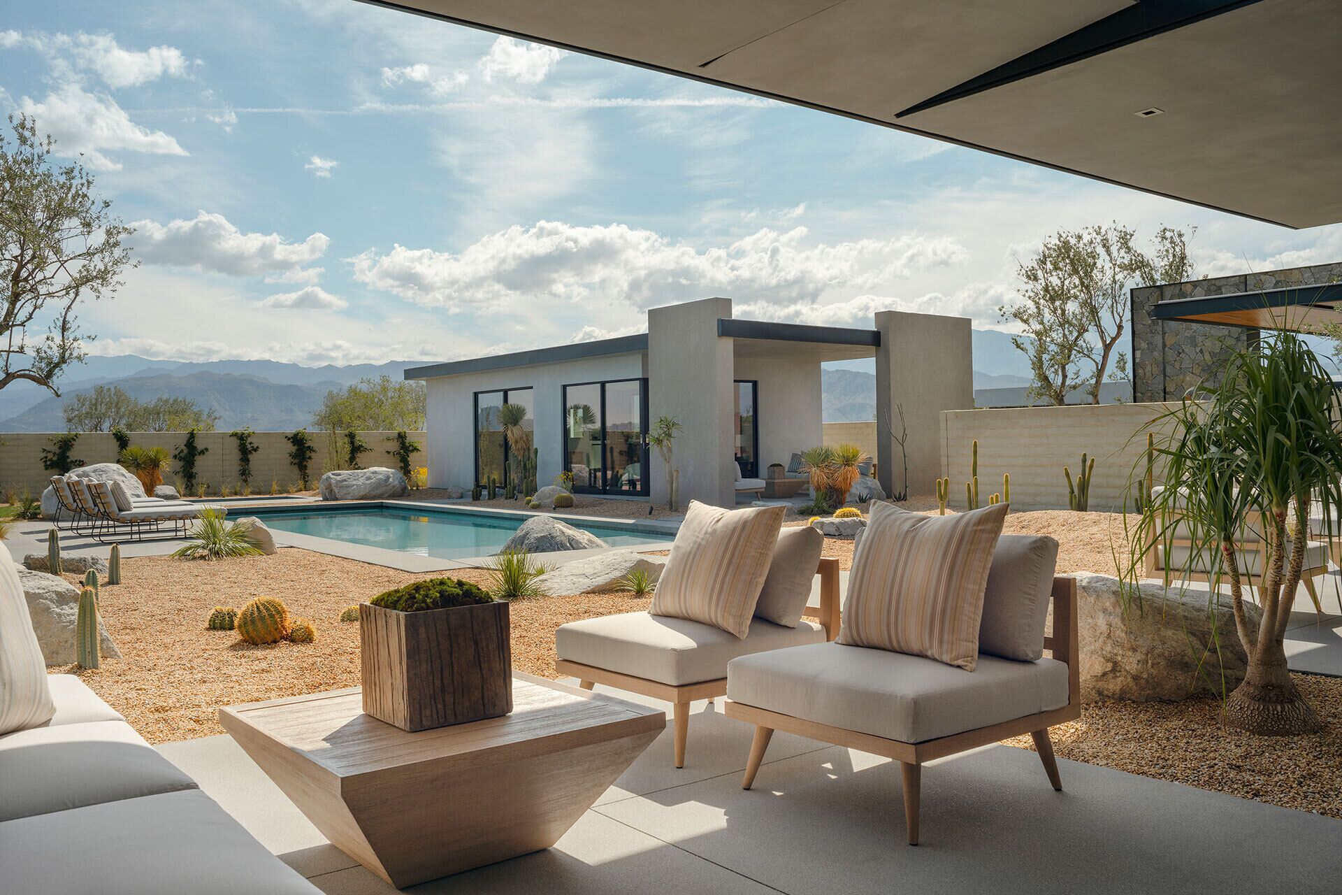 Un'area relax esterna moderna con piscina, sedie a sdraio e vista sulle montagne.