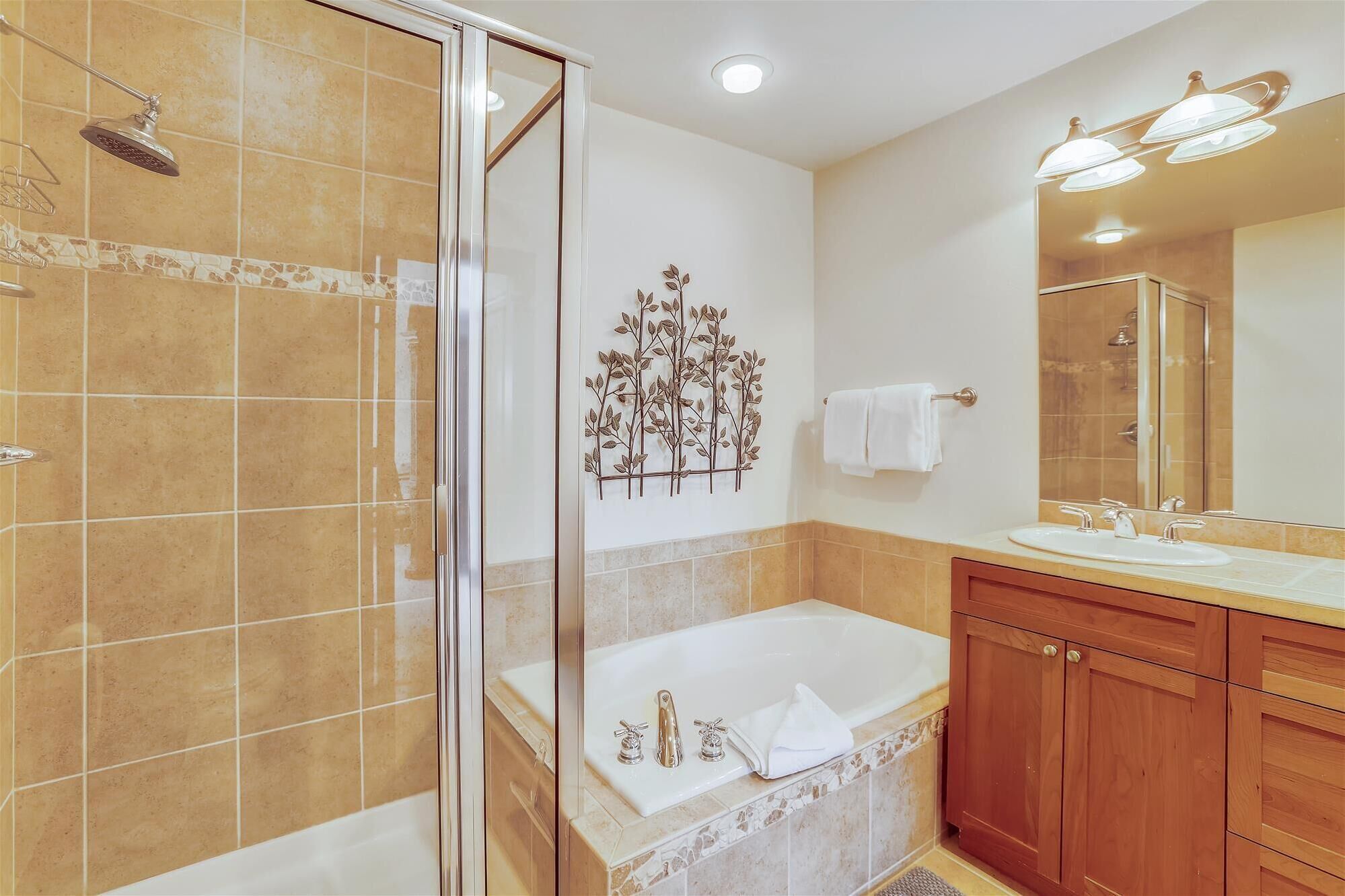 Un baño con cabina de ducha de vidrio, bañera, tocador con espejo y un adorno de pared.