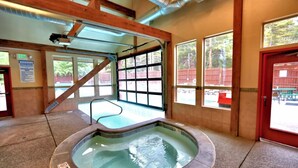 Un jacuzzi en una habitación con ventanas amplias, vigas de madera y una puerta roja.